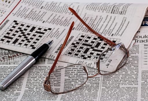 Zeitung mit Kreuzworträtsel. Darauf liegen eine Brille und ein Kugelschreiber.
