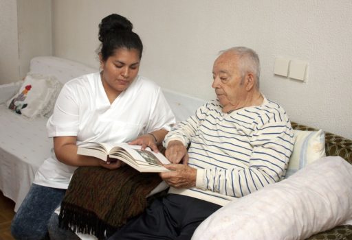 Altenpflegerin blättert mit älterem Mann in einem Buch.